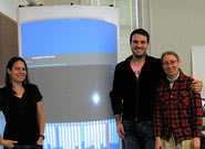 Photo of three people beside curved rear projection screen.
